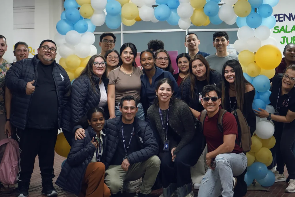 Equipo de la Iglesia Cristo es Vida sonriendo junto a un arco de globos celestes, blancos y amarillos