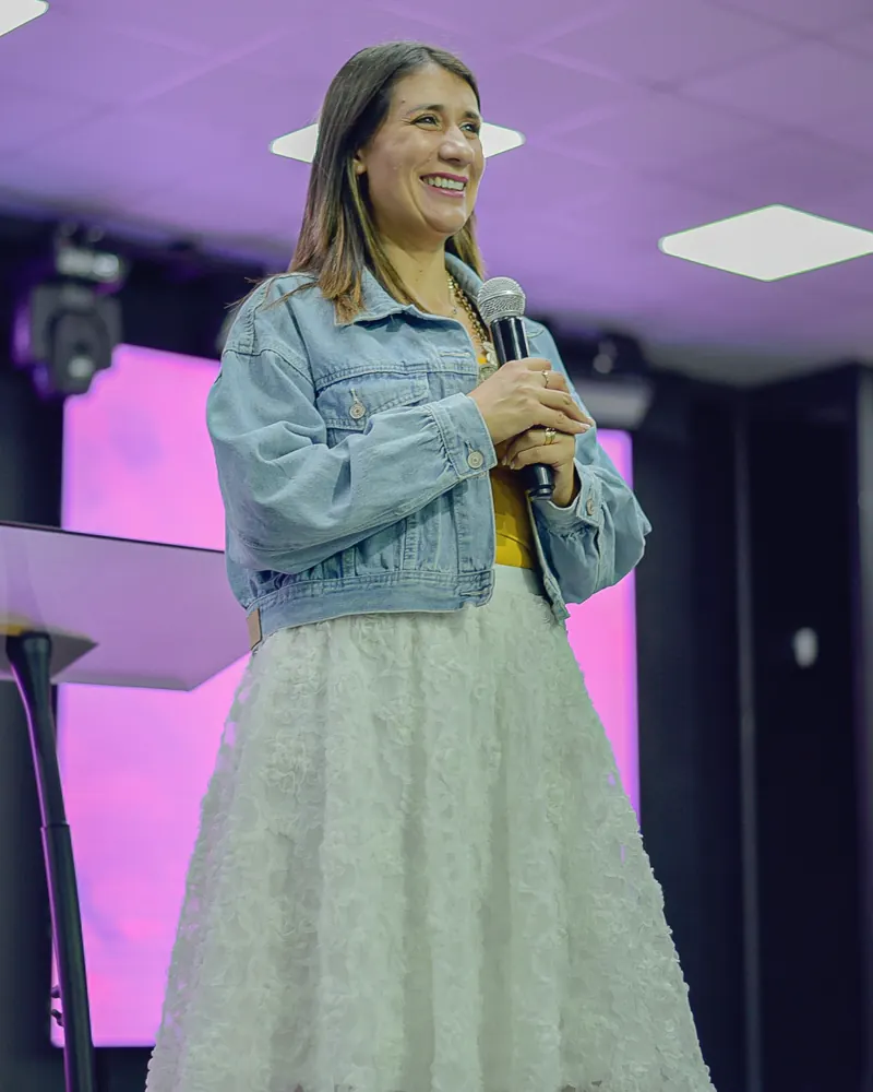 Pastora Carola Briones sonriendo con un micrófono en el escenario de la Iglesia Cristo es Vida